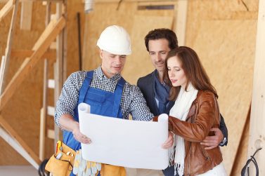 Worker shows house design plans to a young couple at construction site